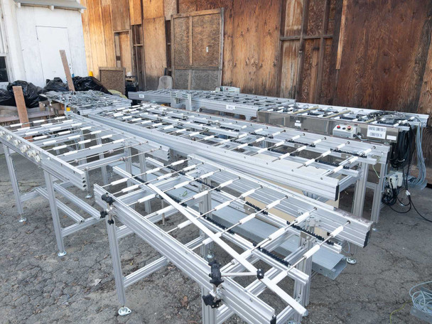 Multiple Excel Flow SC23460 conveyor sections arranged on dirt surface – wide rear-angle view showing roller beds and leg assemblies