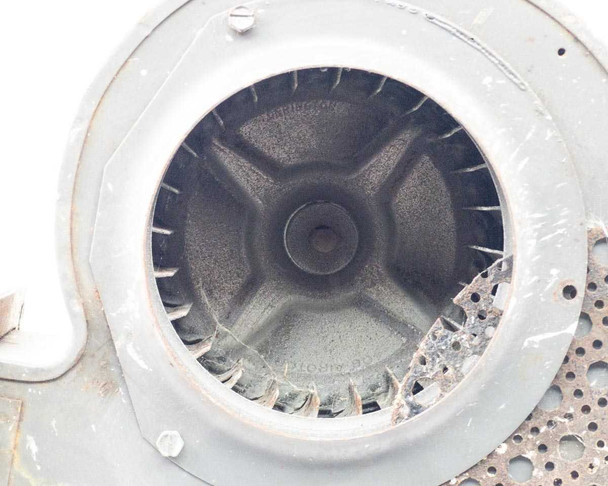Close-up of Torrington blower housing face — interior view through inlet opening showing cast impeller hub and backward-curved blades with accumulated dust and debris; perforated grille partially visible at right