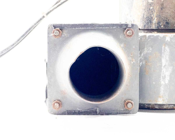 Close-up of Torrington blower square-flanged round tube outlet — face-on view showing open round duct port, four corner bolts on flange plate, surface rust on flange and outlet tube