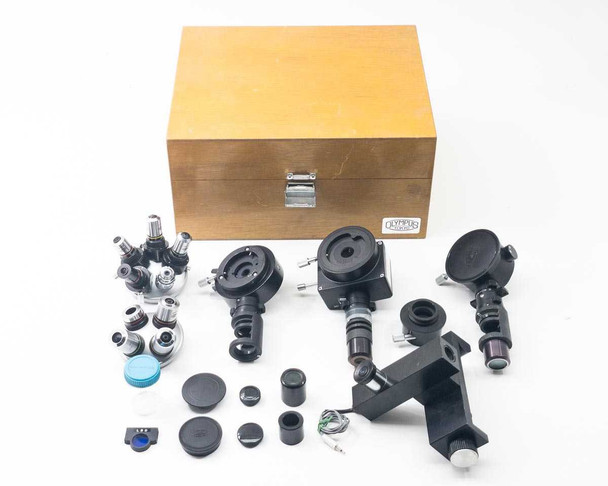 Olympus Tokyo microscope optical component set laid out — wooden storage box, two nosepiece turrets with objectives, filter cube holders, caps, and accessories