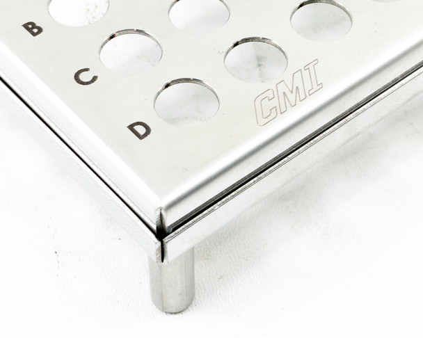 Close-up of CMI stainless steel test tube rack corner — CMI logo etched on frame, rows C and D visible with corner leg detail