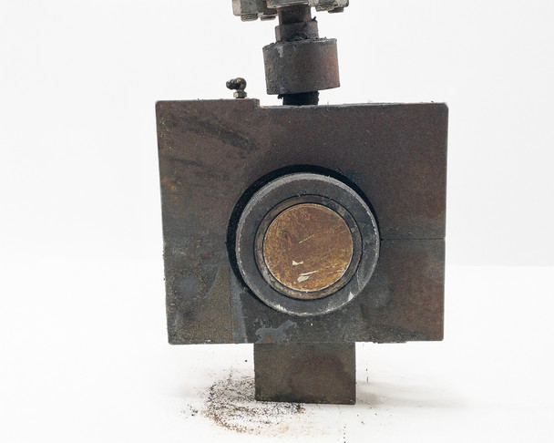 Steel base fixture close-up — face view showing circular bore recess with bronze/copper bushing insert visible, surface rust and debris present