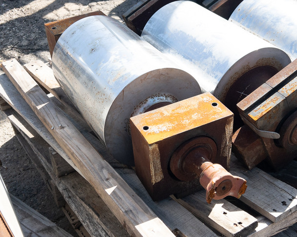 Side view of conveyor drum assembly with yellow hydraulic brake block and shaft stub visible on pallet