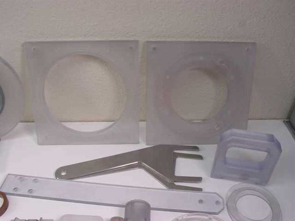 Two clear acrylic square mixer mounting plates with circular cutouts and a stainless steel fork/scraper tool