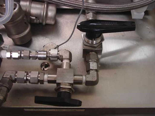 Detail of stainless steel valve manifold with ball valves, needle valves, compression fittings, and black-handled shutoff valve