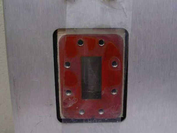Close-up of waveguide port opening with red flange adapter plate showing rectangular waveguide aperture and mounting hole pattern