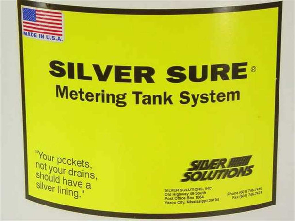 Silver Solutions Silver Sure Metering Tank System – close-up of yellow label on tank reading 'Silver Sure Metering Tank System', Made in U.S.A. flag, Silver Solutions Inc. branding, Yazoo City Mississippi contact information, and tagline 'Your pockets, not your drains, should have a silver lining'