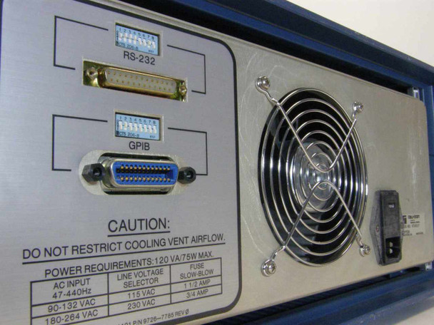 Tau-Tron STX-1101 rear panel close-up showing RS-232 connector, GPIB connector, power requirements label (120VA/75W, 47-440Hz), line voltage selector, fuse holders, and cooling fan