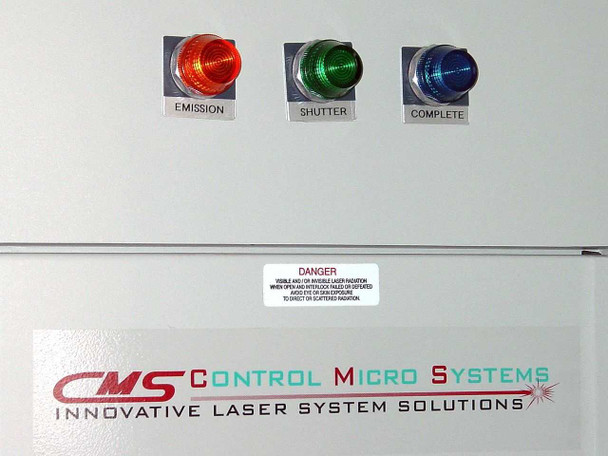 CMS PS-700 front panel indicator lights — three illuminated indicators labeled EMISSION (red), SHUTTER (green), COMPLETE (blue), with CMS Control Micro Systems logo and laser danger warning label
