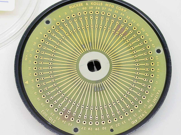 Rucker & Kolls MFG Corp circular PCB test socket — top surface showing numbered gold-plated radial pin contacts (1–60+), center mounting hole, patent marking, and PCB PN 210-003