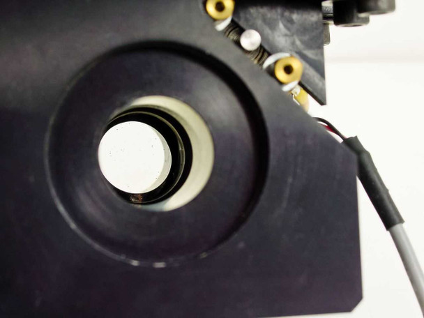 Close-up of shutter aperture showing white circular shutter disc inside anodized housing with solenoid actuator arm and wiring visible