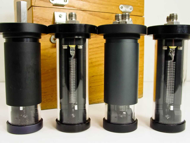 Four Texas Instruments fused quartz Bourdon tube sensor capsules close-up — two with visible coiled quartz tube elements through clear cylinder bodies, two with opaque black cylinders