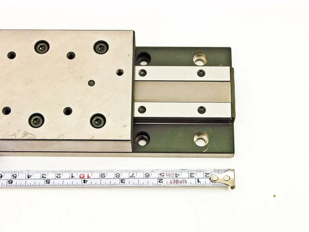 Close-up of dual rail ball-bearing carriage and tapped holes on table surface with measuring tape for scale