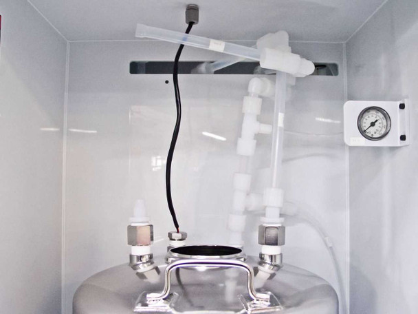 Close-up of top of stainless steel chemical canister inside FSI ChemFill cabinet showing polypropylene inlet/outlet tubing connections, liquid level sensor, and top-mount fittings