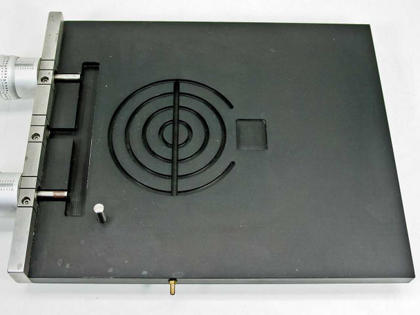 Mitutoyo 197-201 stage — top-down view showing full black anodized platform, concentric target groove pattern, cross slot, and brass vacuum barb fitting at bottom edge
