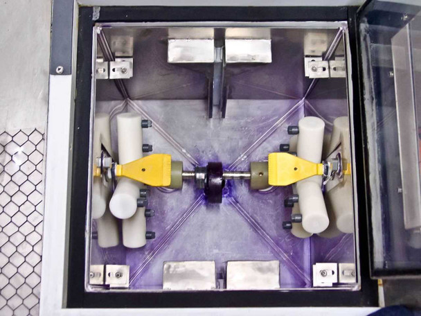 Interior of wafer mask cleaning chamber top-down view showing spray nozzle cross pattern, yellow mask/wafer holders, white roller guides, and stainless steel chamber walls