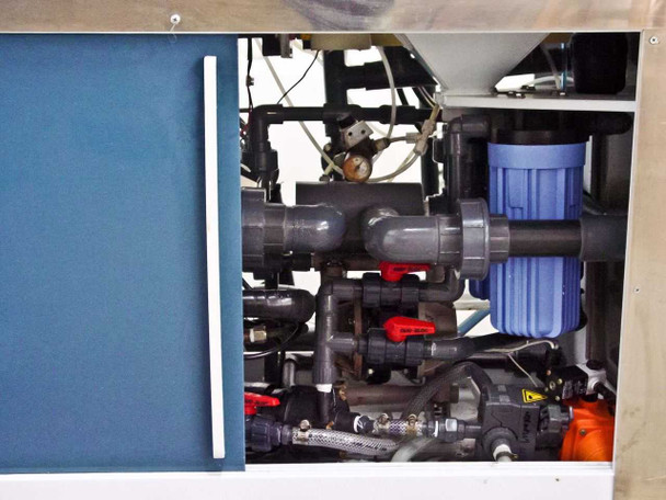 Lower cabinet interior showing fluid plumbing with PVC pipes, blue filter canisters, manual valves with red handles, and chemical routing manifold