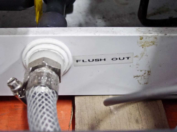 Flush Out connection port on white exterior panel showing braided stainless hose connection and staining/residue on panel surface near port