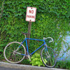 A sleek, modern bicycle leans casually against a bright, reflective traffic control sign made with ORALITE 6700 Engineer Grade Prismatic Reflective Vinyl. The sign, mounted on a sturdy metal pole, features a vibrant yellow background with bold black lettering and symbols that stand out clearly, even in the daylight. The prismatic pattern of the vinyl reflects light brilliantly, ensuring the sign is highly visible from all angles. The bike, with its streamlined design and polished frame, adds a touch of urban style to the scene, highlighting the durability and effectiveness of the reflective vinyl in a real-world setting.