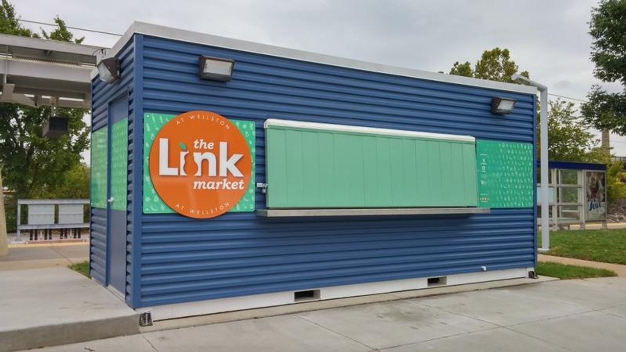 The outside wall of a bustling neighborhood market is wrapped with MacTac Rebel H, showcasing vibrant, high-quality graphics. The textured wall of the market is fully covered with colorful promotional images and text, demonstrating the excellent adhesion and high opacity of the Rebel H film. The graphics look crisp and clear, enhancing the market's exterior appearance.