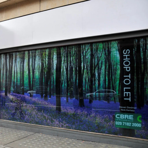 A vibrant, printed graphic mounted on a storefront window, showcasing an eye-catching advertisement. The clear perforated vinyl allows the image to be seen clearly from the outside, drawing attention to the promotion while maintaining visibility from inside the store. The graphic displays bright colors and sharp details, making it an effective tool for retail and point-of-sale campaigns.