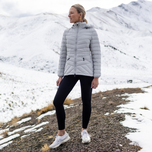 Woman wearing Moke - Cushla Packable Down Jacket (CUSHLA) in the colour Silver on a hill with snow in the background.