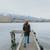 Woman wearing Moke - Arnie Reversible Packable Down Coat (ARNIE) in colour Chocolate/Palomino walking on lake pier.