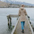 Woman wearing Moke - Arnie Reversible Packable Down Coat (ARNIE) in colour Chocolate/Palomino walking on lake pier.