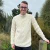 Man leaning on fence wearing Lesley Unisex Aran Wool sweater in the colour Cream.