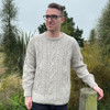 Man leaning on fence wearing Lesley Unisex Aran Wool sweater in the colour Oatmeal.