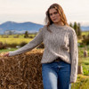 Woman leaning on hay wearing Lesley Unisex Aran Wool sweater in the colour Oatmeal. 