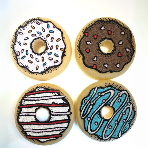 Four donut-shaped sponges displayed together, featuring colorful icing and sprinkle designs.