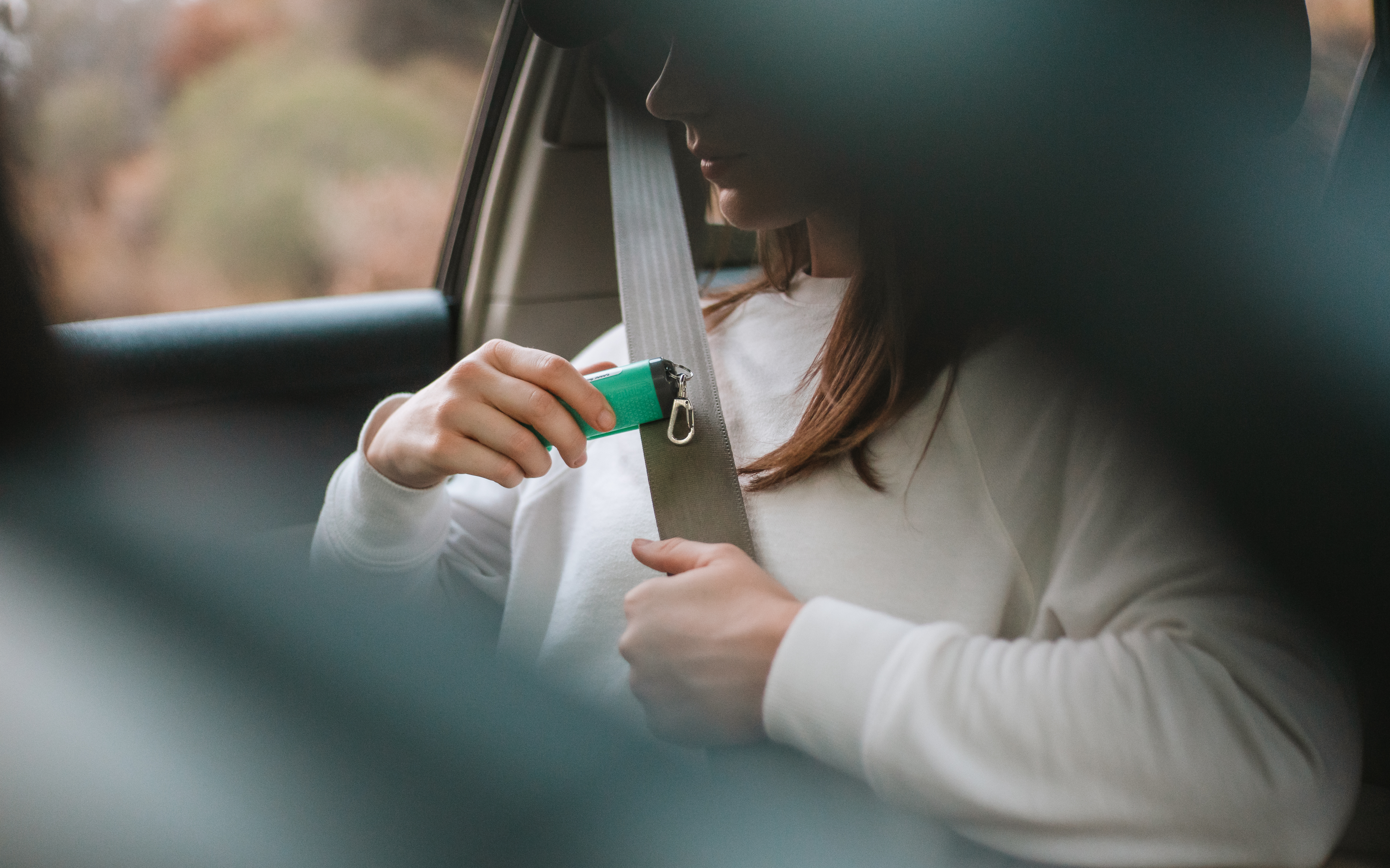 Girl holding personal alarm over seat belt in car 