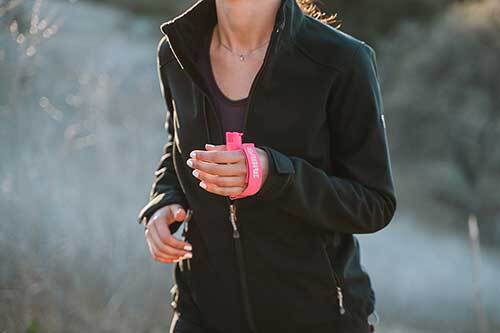 A woman's hand holding a runner pepper gel while running the forest