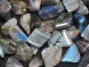 A close-up of an assortment of labradorite tumbled stones lying on a distressed light-colored table. Labradorite is ideal for magickal workings, psychic abilities, astral travel, intuition.