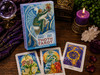 Thoth Tarot Premier Edition box displayed upright with three colorful tarot cards, a purple candle, crystal sphere, quartz cluster, greenery, and ritual accents on a dark wooden surface.