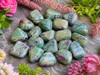 Natural Ruby in Fuchsite tumbled stones with vibrant ruby inclusions displayed among pink flowers in a garden-inspired setting.