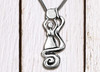 One water witch pewter pendant necklace lying on a light-colored distressed table.