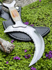 Druids Crescent Moon Bone-Handled Boline rests on the outside of the included leather sheath close-up to show detail of the blade with the sage bundle and incense stick to the left, they are lying on a bed of greenery with purple flowers and wood.