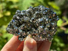Hand holding a top-quality Peruvian pyrite cluster in sunlight, revealing its shimmering golden surface. This crystal is known for grounding, protection, and energizing the solar plexus chakra.