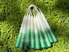 Multiple pairs of white and green ombré beeswax spell candles lying in a bed of sunlit greenery, highlighting their elegant color transition and hand-dipped quality, perfect for prosperity magick and attracting wealth.