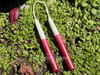 A pair of white and magenta ombré spell candles rest in warm sunlight surrounded by vibrant greenery; these mini taper candles support manifestation magick and personal goal-setting with high vibrational energy.