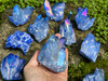 Large Tanzine Aura Quartz cluster crystal held in hand with blue violet aura tones, multiple clusters on rock with greenery background.