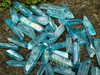 close up of assorted aqua aura quartz points lying on a rock with greenery in the top left corner