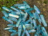 an assortment of aqua aura quartz points lie on a rock with greenery in the upper left corner