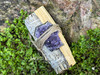 Single smudge kit with white sage, palo santo, and amethyst crystal bundle lying flat on greenery with a natural rock background.