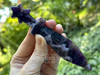 A ChevronDream Amethyst Athame with star-crowned handle held between fingers, multiple amethyst ritual knives in background with greenery setting.