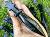 Obsidian crystal athame lying across an open palm showing size and detail, with more obsidian athames in the background resting on greenery.