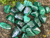 Assorted malachite tumbled stones on a natural rock surface with rich green banding and earthy texture, healing crystals.