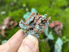 Native copper held between fingers with additional specimens in the background on moss-covered brick, showing depth and raw beauty. Native copper held between fingers with additional specimens in the background on moss-covered brick, showing depth and raw beauty.
